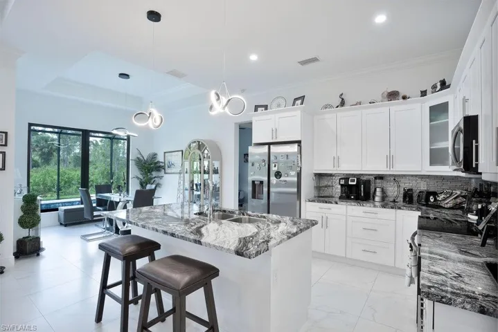 Kitchen featuring hanging light fixtures, a center island with sink, stainless steel appliances, backsplash, and a raised ceiling