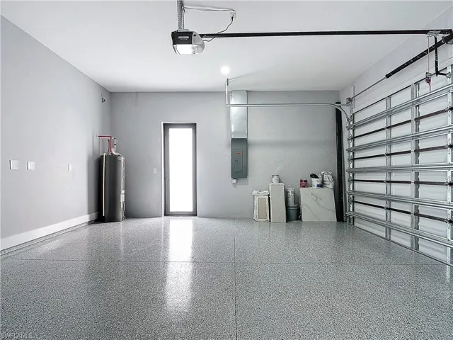Garage with a garage door opener, electric panel, and electric water heater