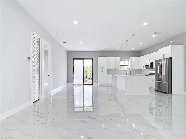 Kitchen with sink, appliances with stainless steel finishes, white cabinets, a center island with sink, and decorative light fixtures