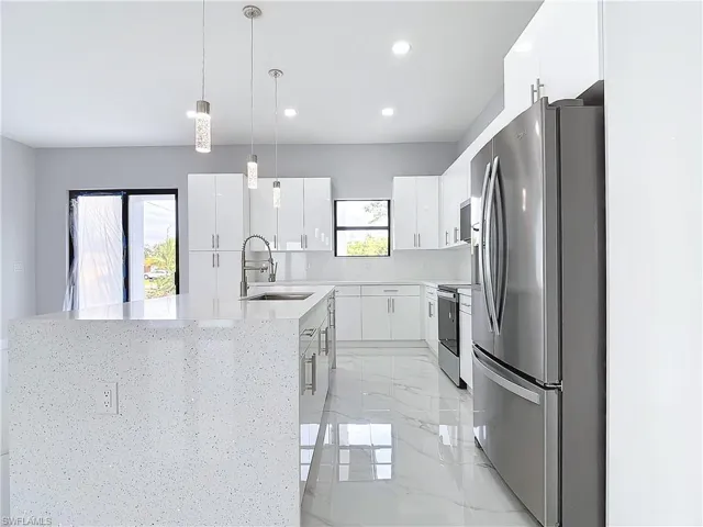 Kitchen with sink, appliances with stainless steel finishes, a kitchen island with sink, white cabinets, and decorative light fixtures
