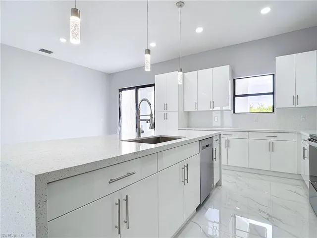 Kitchen with hanging light fixtures, white cabinetry, and sink