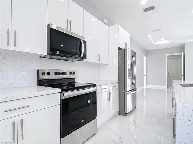Kitchen featuring light stone counters, stainless steel appliances, decorative backsplash, and white cabinets