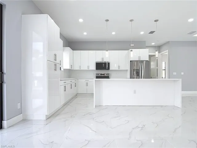 Kitchen with stainless steel appliances, white cabinetry, a center island, and pendant lighting