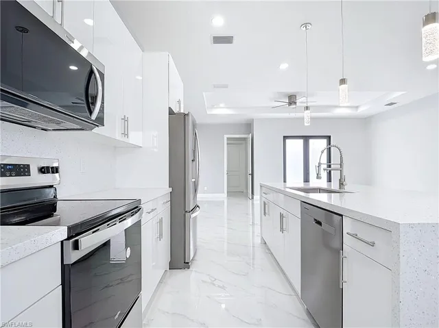 Kitchen with sink, hanging light fixtures, a tray ceiling, stainless steel appliances, and white cabinets