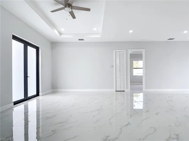 Empty room with a tray ceiling, french doors, and ceiling fan
