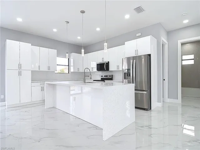 Kitchen featuring sink, white cabinetry, decorative light fixtures, appliances with stainless steel finishes, and an island with sink