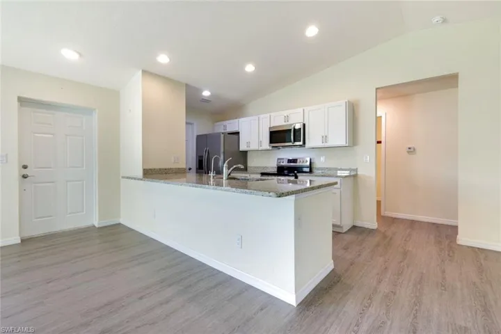 Kitchen featuring recessed lighting, white cabinetry, stainless steel appliances, light wood-style flooring, and light stone counters