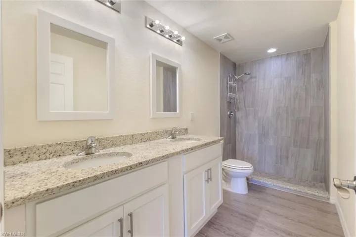 Bathroom featuring double vanity, light wood-style floors, tiled shower, and a textured ceiling
