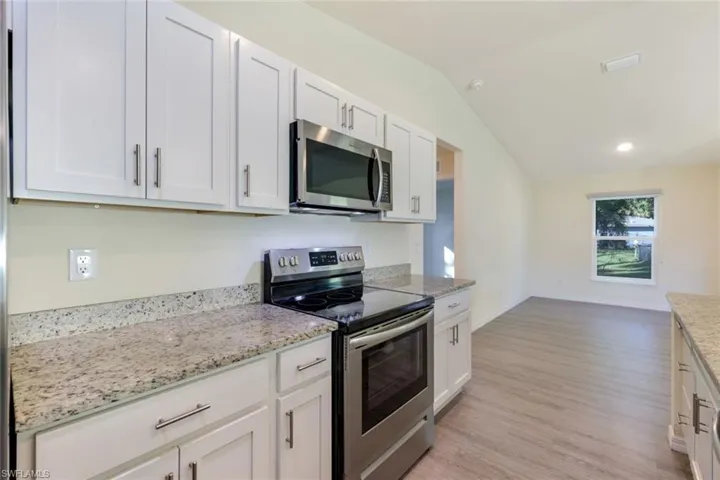 Kitchen with stainless steel appliances, white cabinetry, light stone countertops, light wood-type flooring, and vaulted ceiling