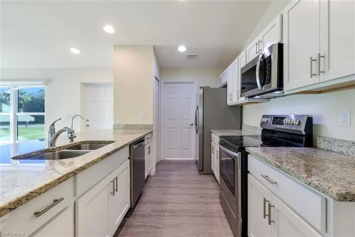 Kitchen featuring appliances with stainless steel finishes, white cabinets, light stone counters, light wood-type flooring, and recessed lighting