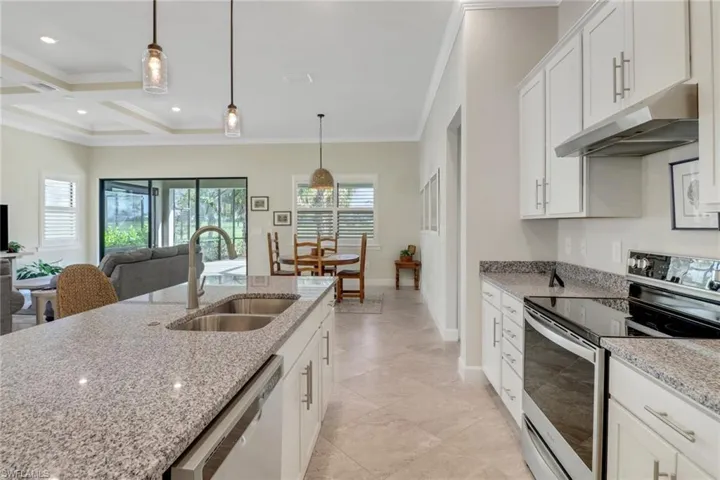 Kitchen featuring appliances with stainless steel finishes, under cabinet range hood, ornamental molding, healthy amount of natural light, and decorative light fixtures