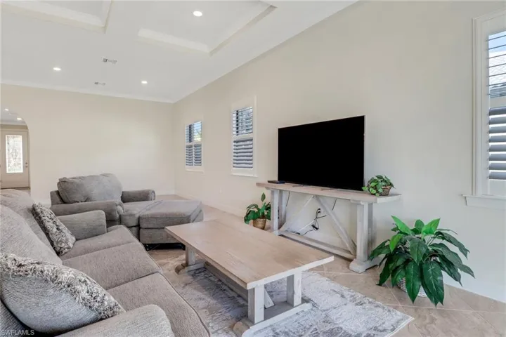 Living area with crown molding, recessed lighting, coffered ceiling, light tile patterned floors, and arched walkways