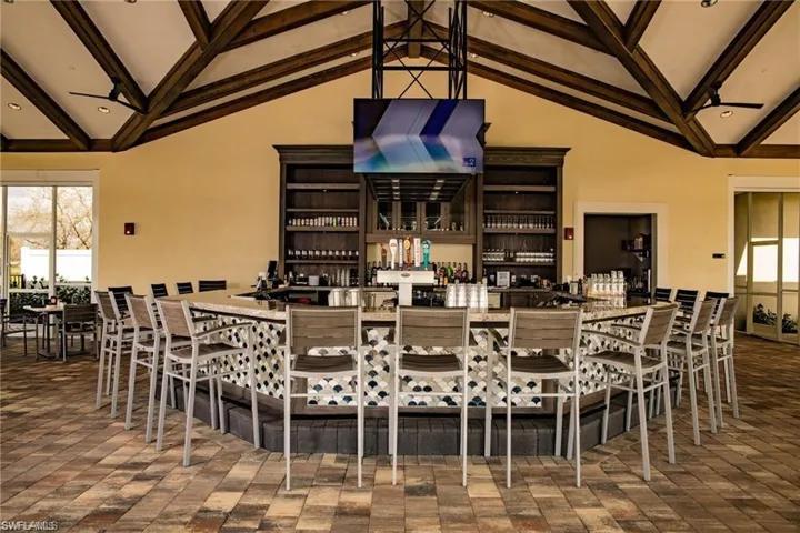 Dining area with beam ceiling, a bar, a ceiling fan, and high vaulted ceiling
