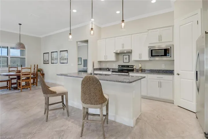 Kitchen with appliances with stainless steel finishes, crown molding, dark stone countertops, pendant lighting, and a kitchen breakfast bar