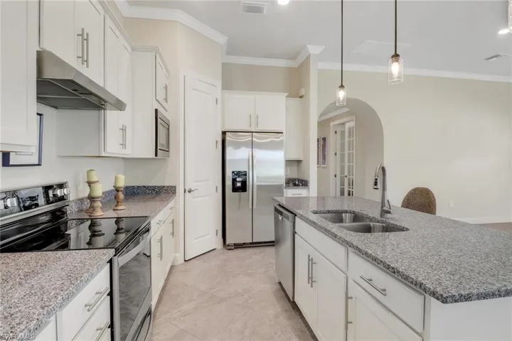 Kitchen featuring appliances with stainless steel finishes, under cabinet range hood, arched walkways, ornamental molding, and white cabinets