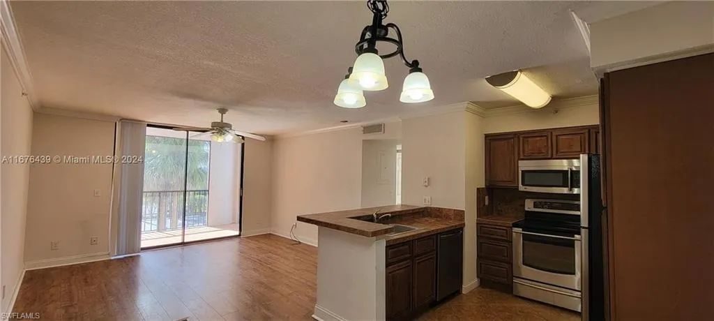 Kitchen featuring pendant lighting, dark wood-type flooring, stainless steel appliances, kitchen peninsula, and ornamental molding