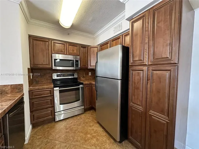 Kitchen featuring tasteful backsplash, ornamental molding, appliances with stainless steel finishes, light tile patterned floors, and a textured ceiling