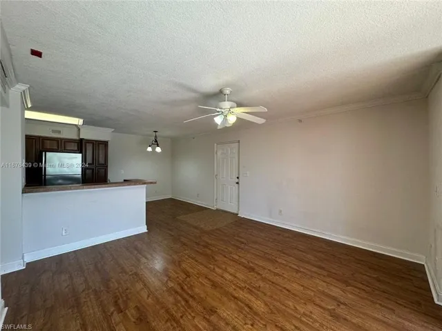 Unfurnished living room featuring crown molding, ceiling fan, dark wood-type flooring, and a textured ceiling