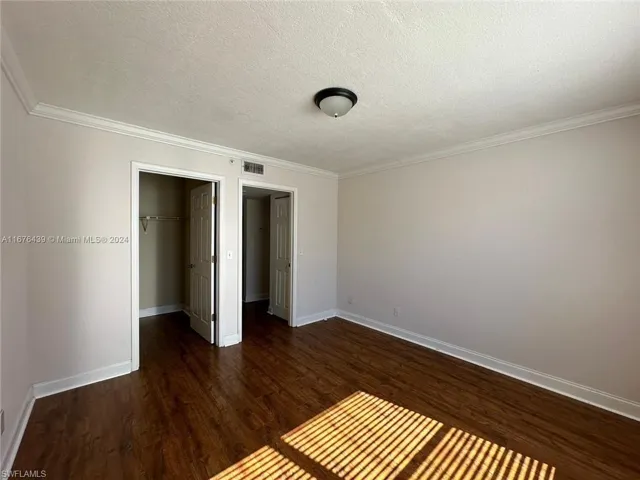 Unfurnished bedroom featuring ornamental molding, a closet, dark hardwood / wood-style floors, and a textured ceiling