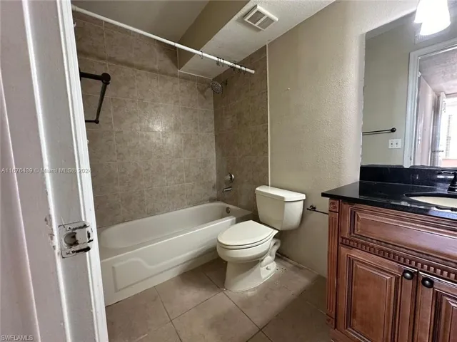 Full bathroom with vanity, tiled shower / bath, tile patterned floors, toilet, and a textured ceiling