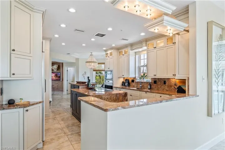 Kitchen featuring stone counters, stainless steel appliances, kitchen peninsula, backsplash, and light tile patterned flooring