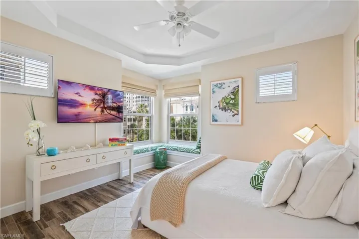 Bedroom with dark wood-type flooring, a tray ceiling, and ceiling fan