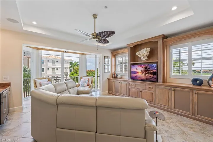 Living room featuring a raised ceiling, light tile patterned floors, and ceiling fan