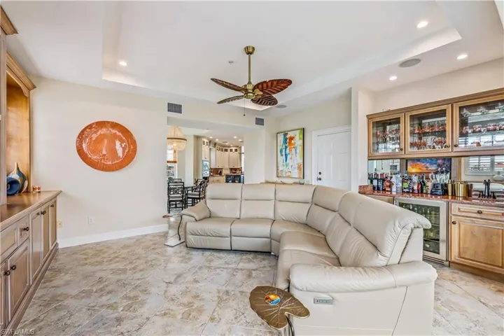 Living room with a raised ceiling, wine cooler, light tile patterned floors, and ceiling fan