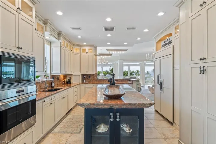 Kitchen with a center island, backsplash, light stone countertops, built in appliances, and sink