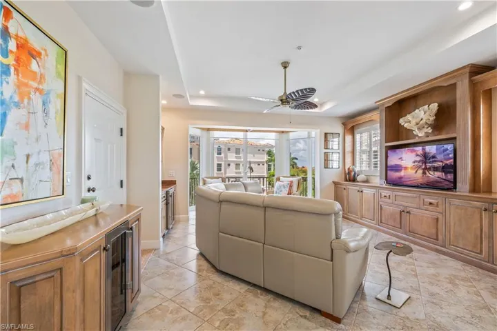 Tiled living room with ceiling fan, wine cooler, and a tray ceiling