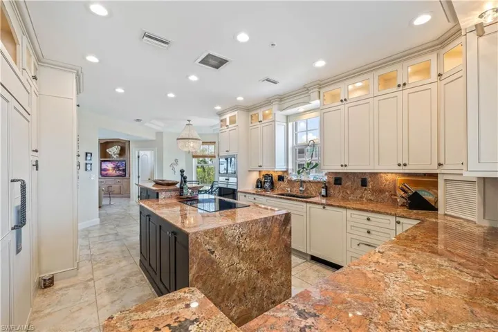Kitchen with sink, backsplash, light tile patterned floors, light stone countertops, and black electric stovetop