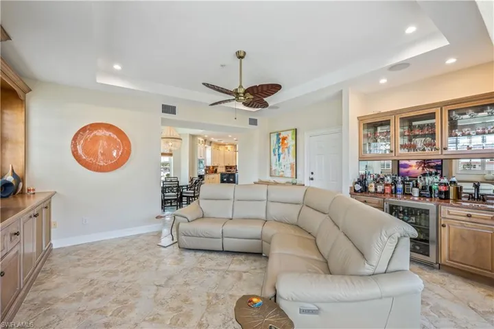 Living room with ceiling fan, a wealth of natural light, light tile patterned floors, a tray ceiling, and wine cooler