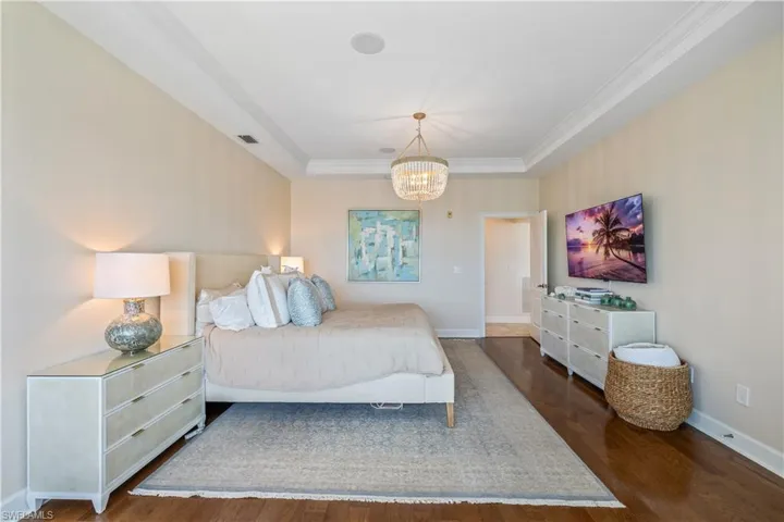 Bedroom with a notable chandelier, a raised ceiling, and dark wood-type flooring