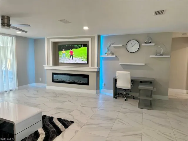 Living area featuring light marble finish flooring, a glass covered fireplace, a ceiling fan, an office area, and recessed lighting