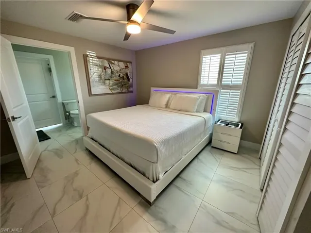 Bedroom with light marble finish flooring, a ceiling fan, and ensuite bath
