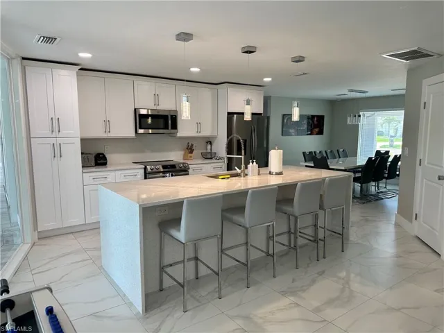 Kitchen featuring a kitchen breakfast bar, light stone counters, hanging light fixtures, a kitchen island with sink, and recessed lighting