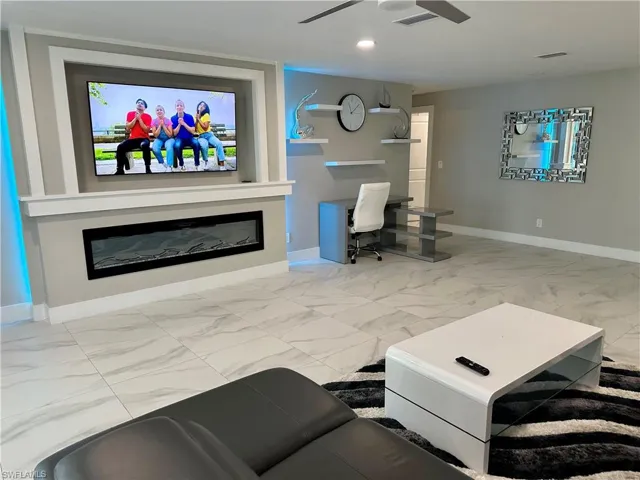 Living room with light marble finish flooring, an office area, a glass covered fireplace, and recessed lighting