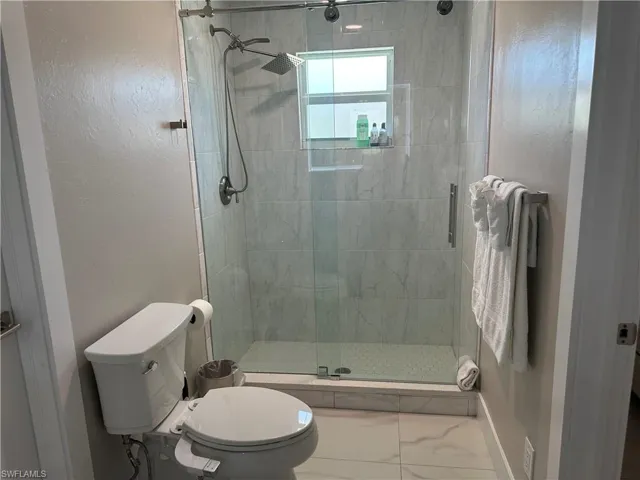 Bathroom featuring a shower stall, marble look tiles, and a textured wall