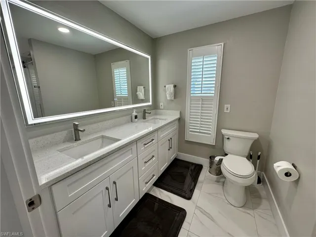 Bathroom featuring double vanity, plenty of natural light, and light marble finish flooring