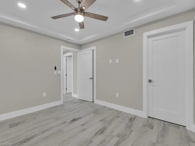 Unfurnished bedroom with a tray ceiling, wood tiled floors, recessed lighting, and a ceiling fan