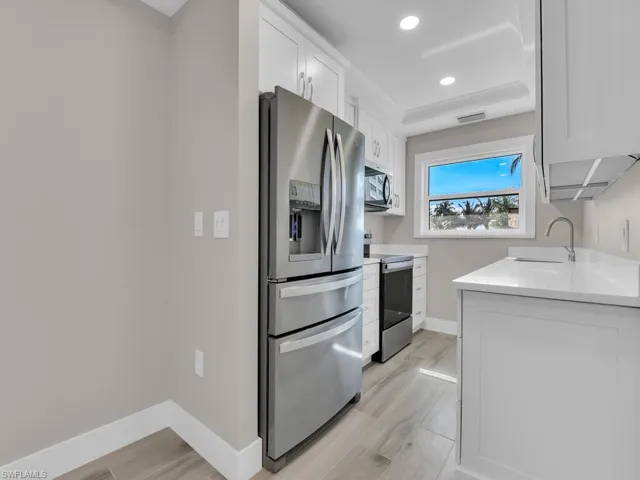 Kitchen with appliances with stainless steel finishes, white cabinetry, light stone counters, recessed lighting, and light wood-style floors