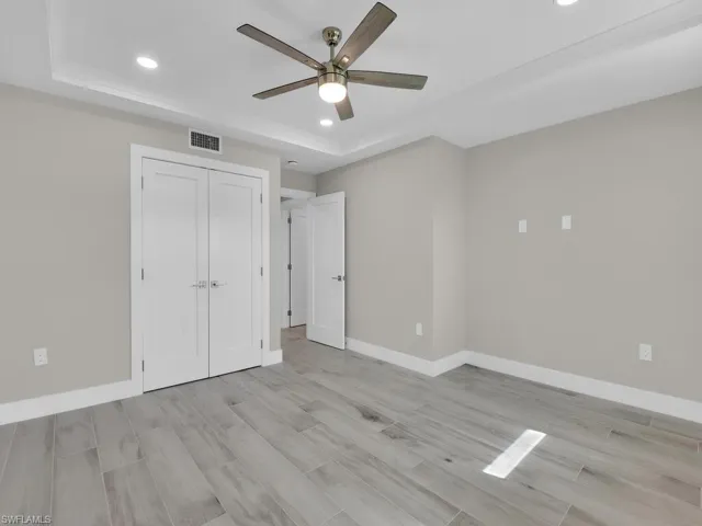 Unfurnished bedroom with recessed lighting, wood finish floors, a tray ceiling, ceiling fan, and a closet