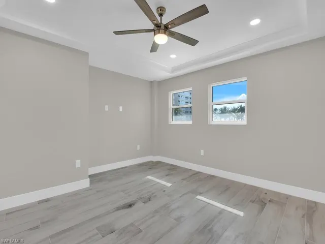 Spare room with a tray ceiling, recessed lighting, light wood finished floors, and ceiling fan