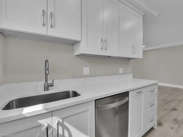 Kitchen with white cabinets, dishwasher, light wood-type flooring, and light stone countertops