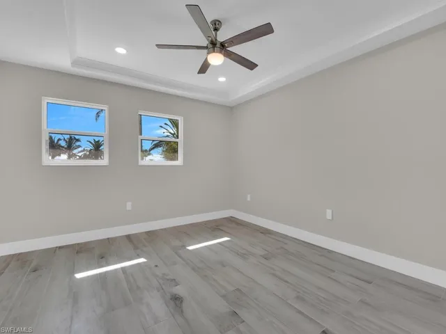 Empty room with a tray ceiling, light wood-style floors, recessed lighting, and a ceiling fan