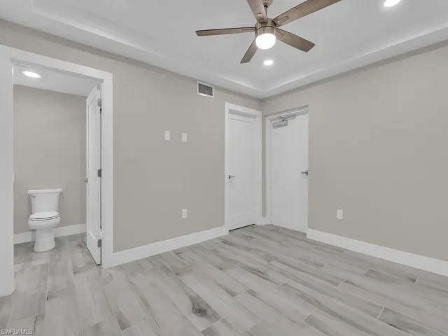 Unfurnished bedroom featuring a raised ceiling, wood finish floors, recessed lighting, a ceiling fan, and ensuite bath