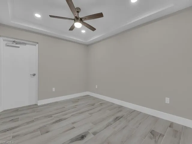 Empty room with a raised ceiling, wood tiled floors, recessed lighting, and a ceiling fan