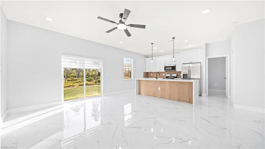 Kitchen with an island with sink, hanging light fixtures, light marble finish flooring, open floor plan, and white cabinets