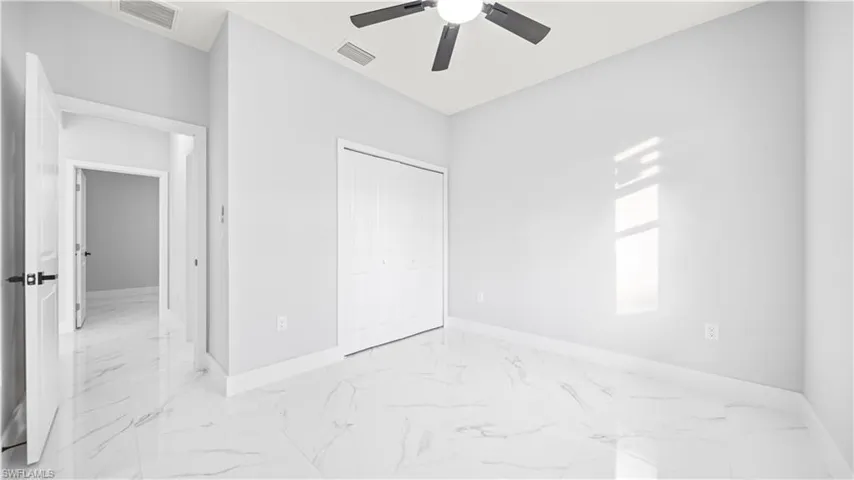 Unfurnished bedroom with light marble finish flooring, a ceiling fan, and a closet