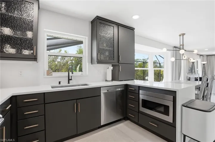 Kitchen with glass insert cabinets, a peninsula, stainless steel appliances, light stone countertops, and pendant lighting - Virtually Edited Image